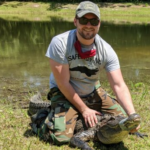 Picture of Thomas Jackson sitting on top of an alligator he is testing. 